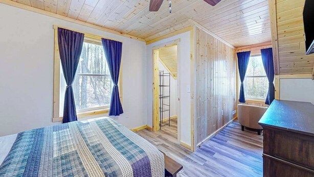 Een kamer met een bed, houten wanden, een plafondventilator en uitzicht door een raam.