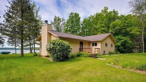 A two-story house with a chimney, a front porch, and a view of a lake. - Lakefront haven with three living areas and WiFi (Manitowish Waters)