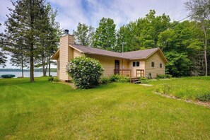 A two-story house with a chimney, a front porch, and a view of a lake. - Lakefront haven with three living areas and WiFi (Manitowish Waters)