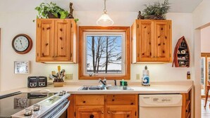 A kitchen with wooden cabinets, a window with a view, a clock, and a dishwasher. - Lakefront haven with three living areas and WiFi (Manitowish Waters)