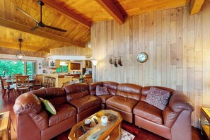 A spacious living area with a large leather sectional sofa, wooden ceiling beams, and a visible kitchen area in the background.