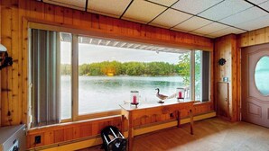 Una cabaña con un ventanal grande que da a un lago, un banco de madera y una mesa con adornos.