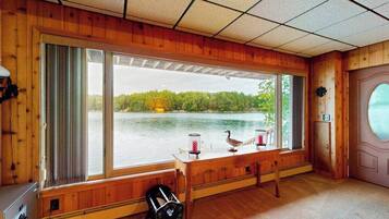 Une cabane dotée d’une grande fenêtre donnant sur un lac, d’un banc en bois et d’une table agrémentée d’objets décoratifs.