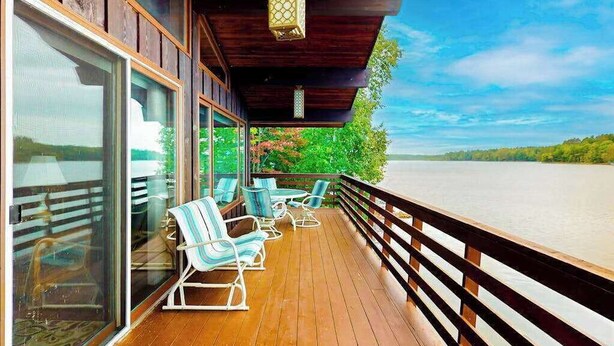 Terraza de madera con mobiliario exterior y vista a un cuerpo de agua.
