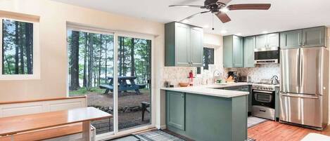 Una cocina moderna con una isla central, electrodomésticos integrados y vistas a zona boscosa.