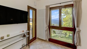 Ein Zimmer mit einem großen Fenster, einem Heizkörper, einem Regal mit Dekoration und einer Tür zu einem Außenbereich.