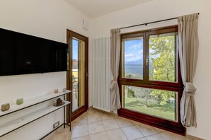 A room with a large window, a radiator, a shelf with decorative items, and a door leading to an outdoor area. - MGH - My Lakeview Escape (Peschiera del Garda)
