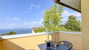 Ein Balkon mit Tisch für zwei Personen, einer Flasche und Gläsern mit Blick auf Wasser und Grünflächen.