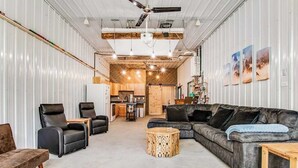 A spacious living area with a sofa, chairs, a coffee table, and a kitchen in the background. - Barn & cabin with firepits, grills, foosball, kayaks, home theater, & 2 kitchens (Necedah)