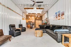 Un grand espace de vie comprenant un canapé, des fauteuils, une table basse et une cuisine en arrière-plan.