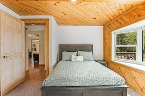 Une chambre avec un plafond en bois, une grande fenêtre et un lit recouvert d’une couverture verte.
