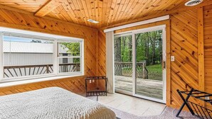 A wooden cabin room with a bed, a bench, and a sliding glass door to a deck. - Barn & cabin with firepits, grills, foosball, kayaks, home theater, & 2 kitchens (Necedah)