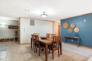 A dining area with a wooden table and chairs, a ceiling light, and a blue accent wall with woven wall art.