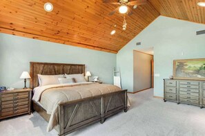 A bedroom with a wooden ceiling, a bed, a nightstand, a dresser, and a door.