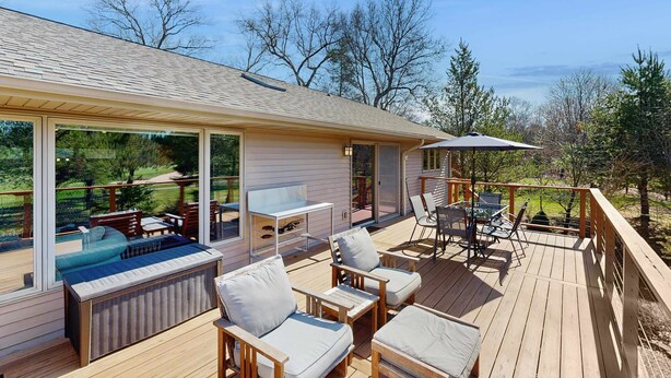A deck with outdoor seating, a table, and a glass enclosure. - Green side smart home with golf, beach/lake access, off-site dock & EV charger (Nekoosa)