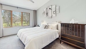 A bedroom with a large bed, a ceiling fan, a dresser, and a view of trees through the window. - Green side smart home with golf, beach/lake access, off-site dock & EV charger (Nekoosa)