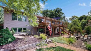 A two-story house with a deck, outdoor seating, and a flag. - Green side smart home with golf, beach/lake access, off-site dock & EV charger (Nekoosa)