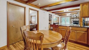 A dining area with a round wooden table and chairs, wooden beams on the ceiling, and a kitchen with wooden cabinets and a stone countertop. - Cozy wooded duplex w/ WiFi, full kitchen, shared W/D & near lakes & trails (Arkdale)