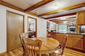 A dining area with a round wooden table and chairs, wooden beams on the ceiling, and a kitchen with wooden cabinets and a stone countertop. - Cozy wooded duplex w/ WiFi, full kitchen, shared W/D & near lakes & trails (Arkdale)