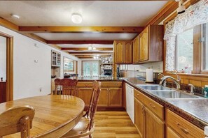 A kitchen with wooden cabinets, a granite countertop, and a dining area with a wooden table and chairs. - Cozy wooded duplex w/ WiFi, full kitchen, shared W/D & near lakes & trails (Arkdale)