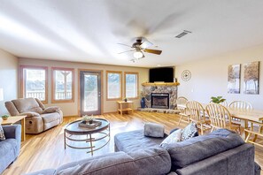 A spacious living room with a fireplace, a ceiling fan, and a dining area with wooden furniture.