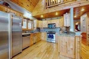 A wooden cabin-style kitchen with a refrigerator, stove, microwave, and wooden cabinets.