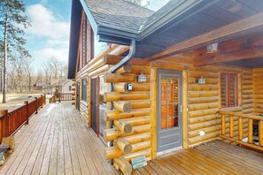 A log cabin with a wooden deck, a door with a window, and a mailbox.