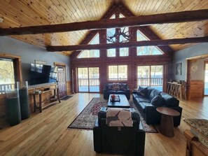A spacious living room with a large wooden ceiling, a fireplace, a television, and a sofa.