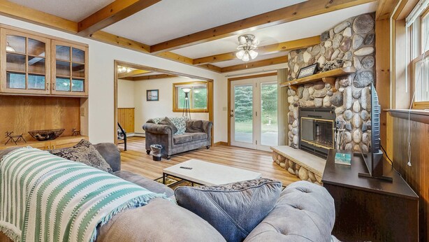 A spacious living room with a fireplace, wooden beams, and a stone wall. - Two-family retreat with 2 kitchens, wooded charm near lakes, trails & adventure (Arkdale)