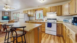 A kitchen with wooden cabinets, a central island, a stove, and a refrigerator. - Two-family retreat with 2 kitchens, wooded charm near lakes, trails & adventure (Arkdale)