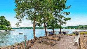 A lakeside picnic area with benches, a picnic table, and a view of the lake. - Waterfront condo with resort amenities, grill, firepit, jetted tub, & partial AC (Wisconsin Dells)