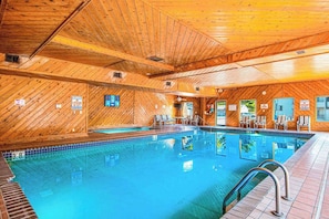 An indoor swimming pool with wooden walls and ceiling, surrounded by lounge chairs.