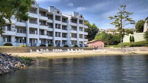 A multi-story hotel with balconies, a pool area with lounge chairs, and a small building in the background. - Waterfront condo with resort amenities, grill, firepit, jetted tub, & partial AC (Wisconsin Dells)