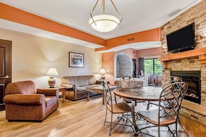A living room with a fireplace, a dining table with chairs, a sofa, and a television mounted on the wall.