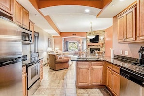 A spacious kitchen with wooden cabinets, a large island, and a stone fireplace.