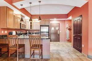 A kitchen with wooden cabinets, a refrigerator, and pendant lighting. - Serene river-view condo + perks + two fireplaces (Wisconsin Dells)