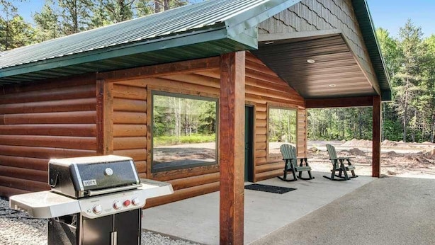Een blokhut met een barbecue, buitenmeubilair en een overdekt terras.