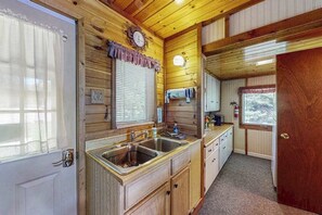 A wooden cabin interior with a kitchen area, including a sink, cabinets, and a clock. - Two cozy, lakefront cottages w/ 2 docks, a patio, firepit, 2 gas grills, & WIFI (Eagle River)