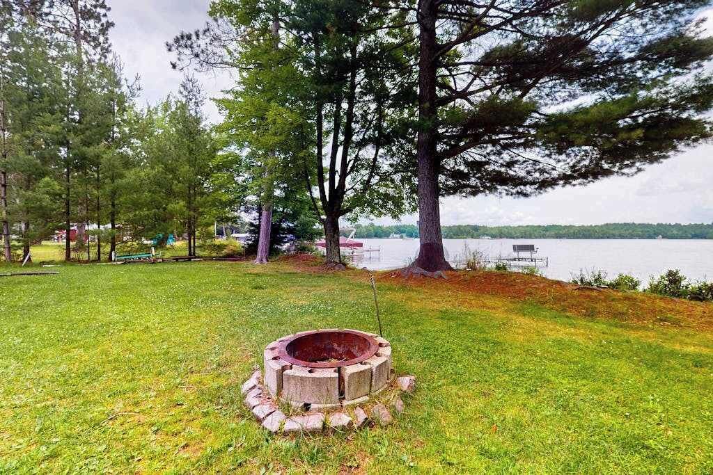 A grassy area with a fire pit, trees, and a lake in the background.