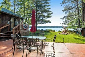 A wooden cabin with a patio, a swing set, and a view of a lake. - Two cozy, lakefront cottages w/ 2 docks, a patio, firepit, 2 gas grills, & WIFI (Eagle River)
