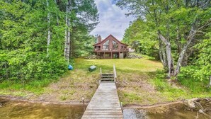 A wooden dock leading to a house surrounded by dense forest.