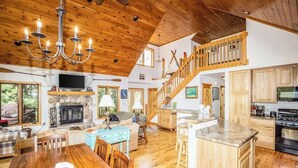 A spacious living area with a fireplace, wooden ceiling, and a staircase leading to an upper level.