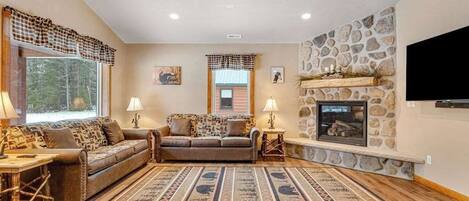 A living room with a stone fireplace, two sofas, a patterned rug, and a television mounted on the wall.