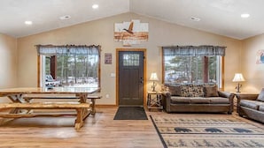 A spacious living room with a wooden table, two sofas, and a large window with a view of trees. - Modern dog-friendly cabin with hot tub, gas fireplace, patio, grill, & AC (Conover)