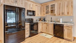 A kitchen with wooden cabinets, a stainless steel refrigerator, a stove, and a dishwasher. - Modern dog-friendly cabin with hot tub, gas fireplace, patio, grill, & AC (Conover)