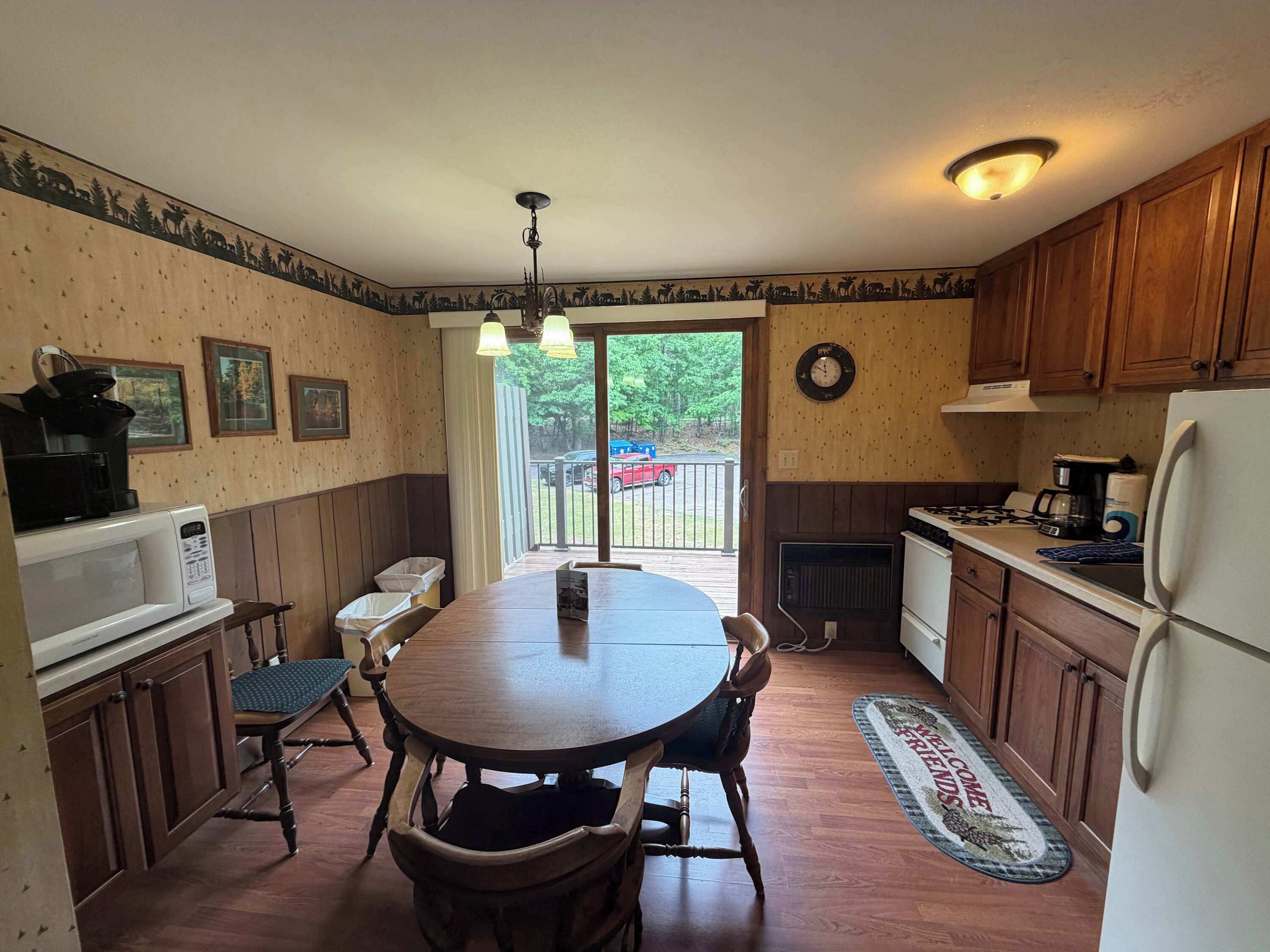 A kitchen with a dining table, chairs, wooden cabinets, a microwave, stove, and a clock on the wall.