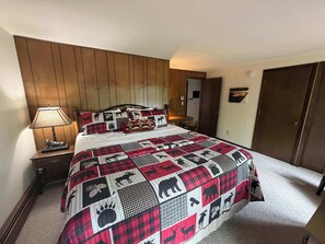 A bedroom with a wooden headboard, a bed with a red and black quilt, a nightstand with a lamp, and a wardrobe.