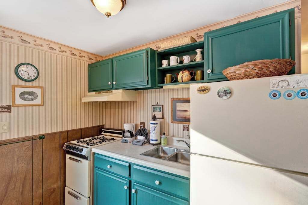 Une cuisine avec des armoires de couleur turquoise, un réfrigérateur blanc, une cuisinière et un évier.