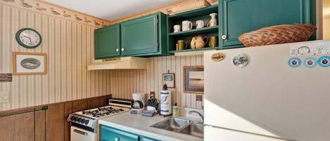 Une cuisine avec des armoires de couleur turquoise, un réfrigérateur blanc, une cuisinière et un évier.