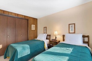 A room with two beds, wooden paneling on the walls, and framed pictures on the wall.